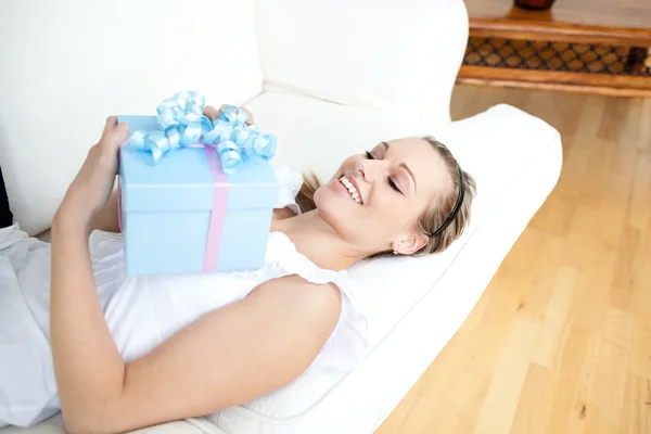 Affascinante donna bionda che tiene un regalo sdraiato su un divano — Foto Stock