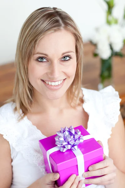 Charming young woman holding a present sitting on the floor — Stock Photo, Image