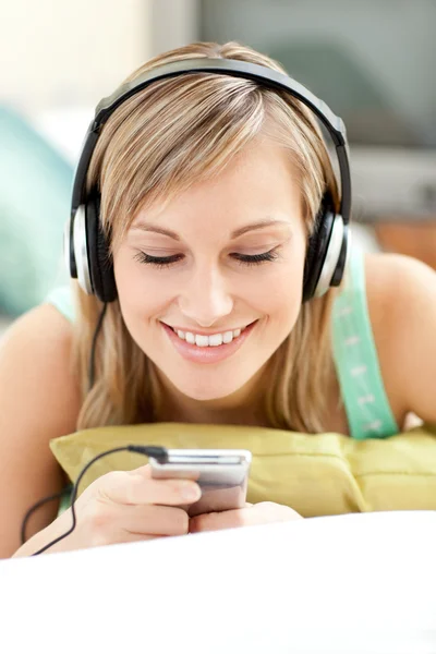 Mujer joven sonriente escuchando música tumbada en un sofá — Foto de Stock
