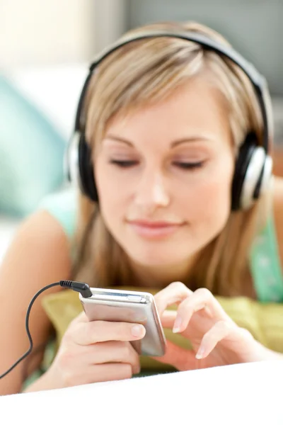 Pretty young woman listening music lying on a sofa — Stock Photo, Image