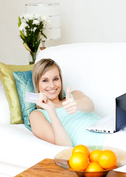 Успешная женщина делает покупки он-лайн лежа на диване — стоковое фото