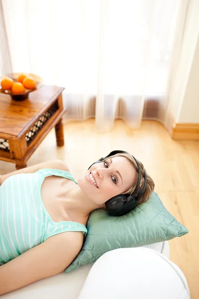 Allegro donna bionda ascoltare musica sdraiata su un divano — Foto Stock