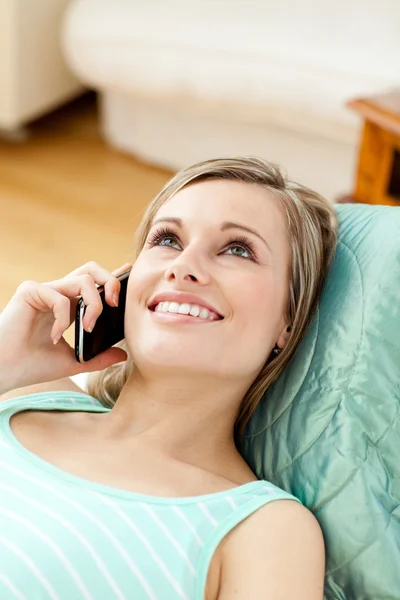 Χαμογελώντας νεαρή γυναίκα μιλάει στο τηλέφωνο που βρίσκεται σε έναν καναπέ — Φωτογραφία Αρχείου