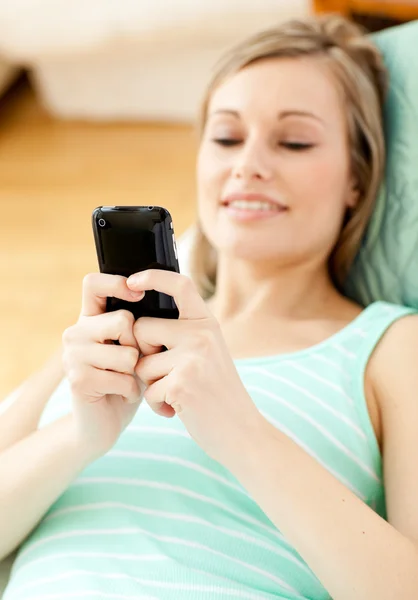 Ljusa ung kvinna skicka en text liggande på en soffa — Stockfoto