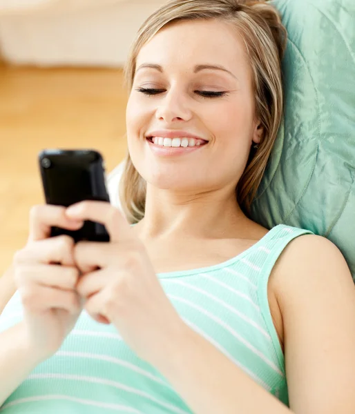 Χαμογελώντας νεαρή γυναίκα που στέλνει ένα κείμενο που βρίσκεται σε έναν καναπέ — Φωτογραφία Αρχείου