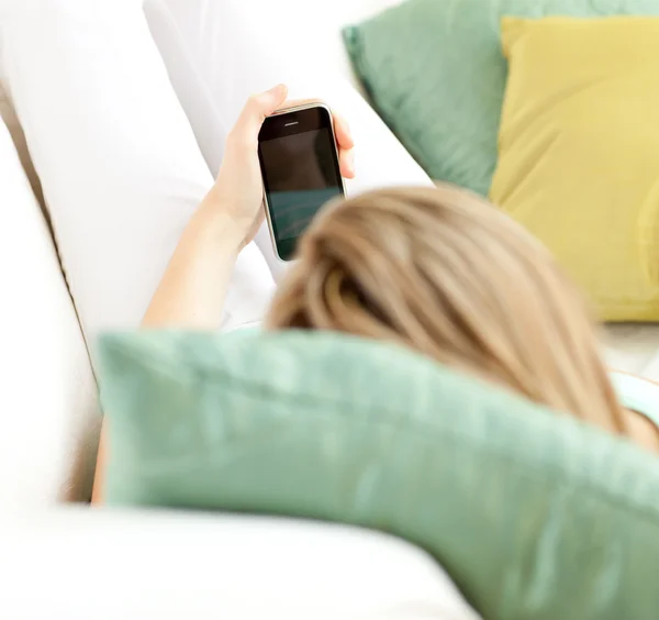 Mujer rubia enviando un mensaje de texto tumbado en un sofá —  Fotos de Stock
