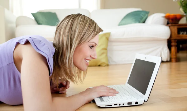 Lächelnde blonde Frau mit Laptop auf dem Boden liegend — Stockfoto