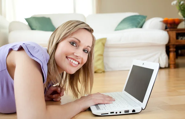 Lustige blonde Frau mit einem Laptop auf dem Boden liegend — Stockfoto