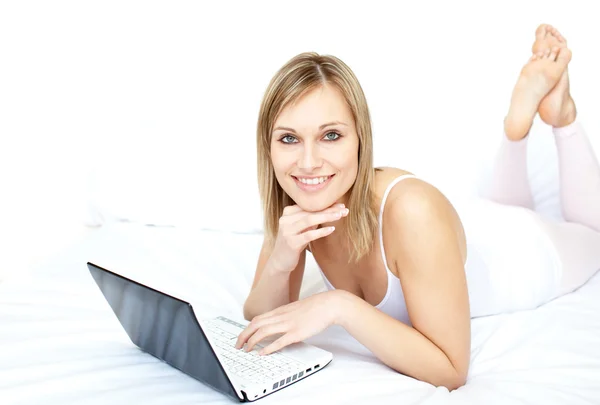 Glad kvinna med en laptop liggande på hennes säng — Stockfoto