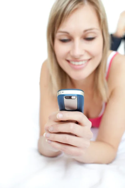Mujer joven enviando un mensaje de texto acostado en una cama — Foto de Stock