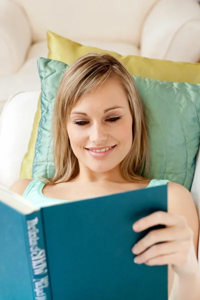 Smiling woman reading a book lying on a sofa — Stock Photo, Image