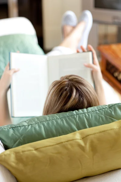 Mulher loira lendo um livro deitado em um sofá — Fotografia de Stock