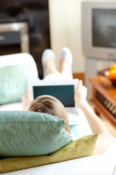 Mulher loira usando um laptop deitado em um sofá — Fotografia de Stock