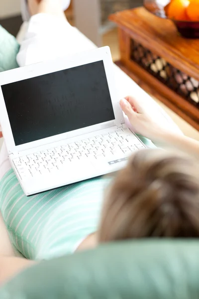 Uma mulher usando um laptop deitado em um sofá — Fotografia de Stock