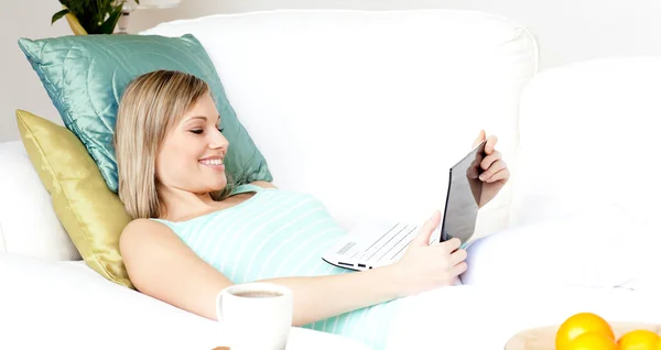 Mulher feliz usando um laptop deitado em um sofá — Fotografia de Stock