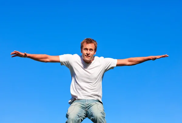 Smiling man jumping against a blue background — Stock Photo, Image