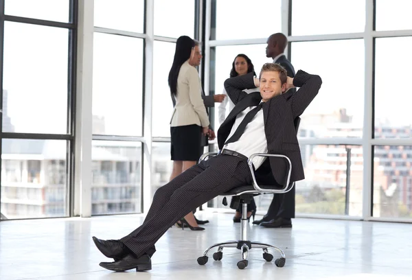Gerente relaxante no escritório com a equipe em segundo plano — Fotografia de Stock