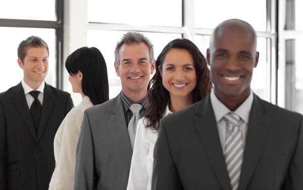 Lächelnder Geschäftsmann blickt in die Kamera mit Gruppe im Hintergrund — Stockfoto