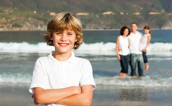 Χαριτωμένο αγόρι σε μια παραλία με τους γονείς του στο παρασκήνιο — Φωτογραφία Αρχείου