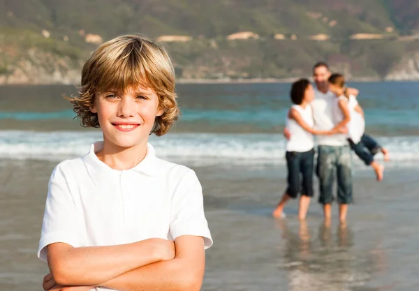 Söt pojke på en strand med sina föräldrar i bakgrunden — Stockfoto