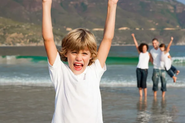 Mignon garçon sur une plage avec ses parents et sa sœur en arrière-plan — Photo