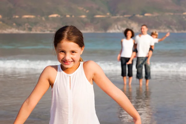 Linda chica en una playa con sus padres y su hermano en el fondo —  Fotos de Stock