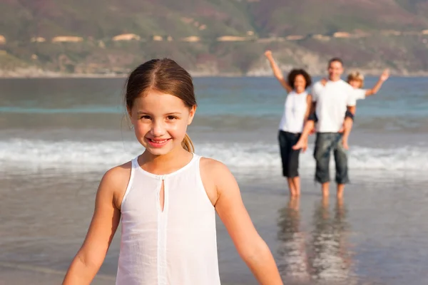 Jolie fille sur une plage avec ses parents et son frère en arrière-plan — Photo