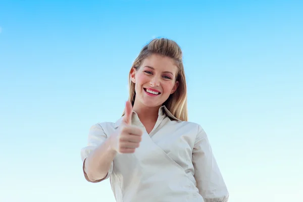 Affärskvinna som ler mot kameran med tummen upp mot blå s — Stockfoto