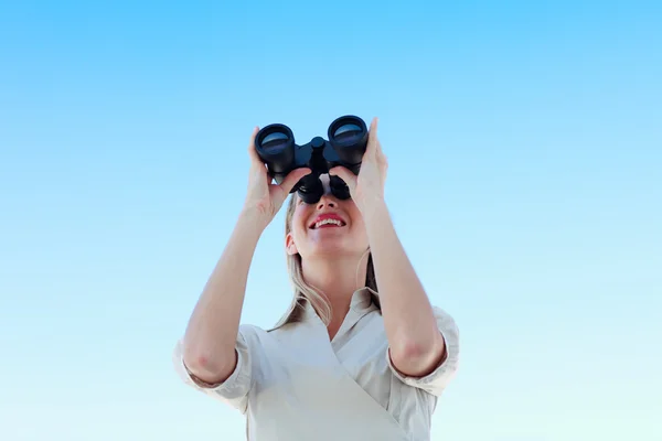 Businesswoman looking through binoculars against blue sky — Stock Photo, Image