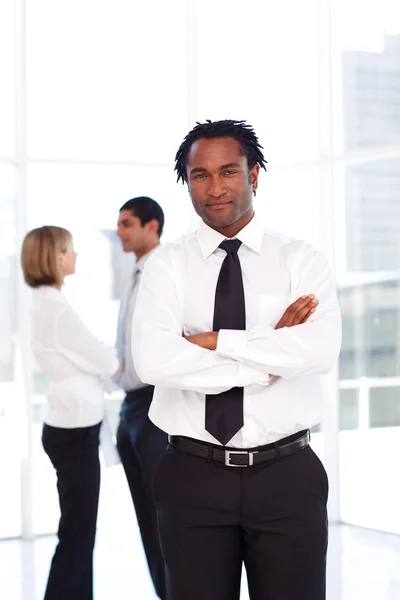 African businessman with folded arms with his team in the backgr — Stock Photo, Image