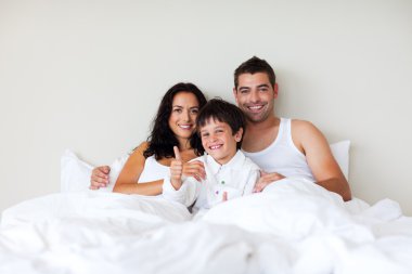 Child with thumbs up and his parents in bed clipart