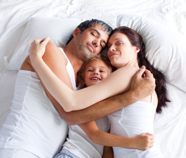 Little gril relaxing on bed with her parents clipart