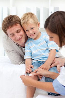 Doctor applying a plaster on a smiling boy's knee clipart