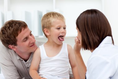 Doctor examining a little boy with his father in tow clipart