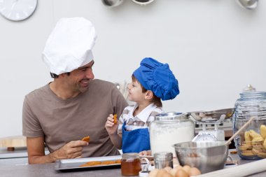 Smiling father and son eating home-made cookies clipart