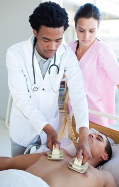 Ethnic doctor using a defibrillator on a patient clipart