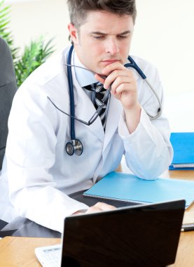 Worried male doctor using a laptop clipart