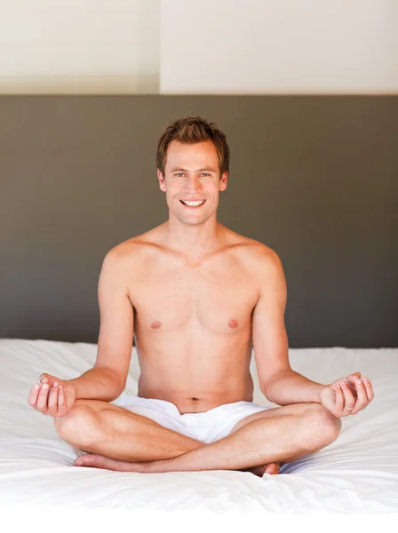 Lachende knappe man mediteren op bed — Stockfoto