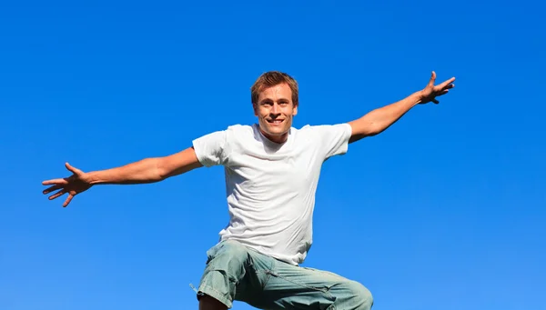 Молодой человек прыгает в воздух против синего неба — стоковое фото