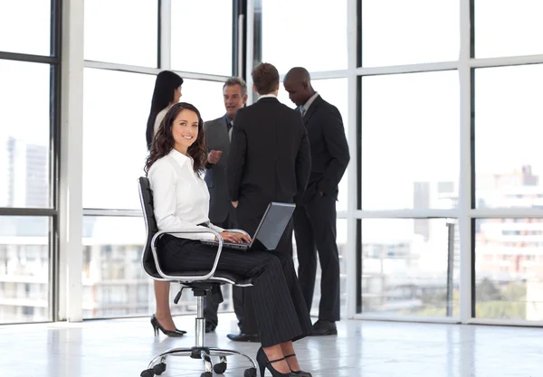 Mulher sentada no escritório trabalhando com equipe em segundo plano — Fotografia de Stock