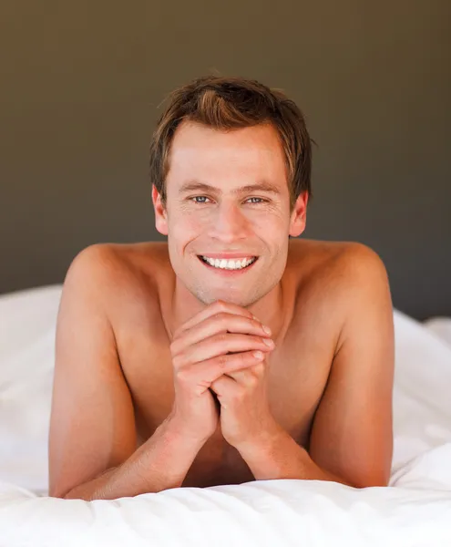 Νεαρός άνδρας ξεκούραστη στο κρεβάτι να χαμογελά στη φωτογραφική μηχανή — Φωτογραφία Αρχείου