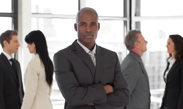 Seriöser Geschäftsmann blickt in Kamera mit Gruppe im Hintergrund — Stockfoto
