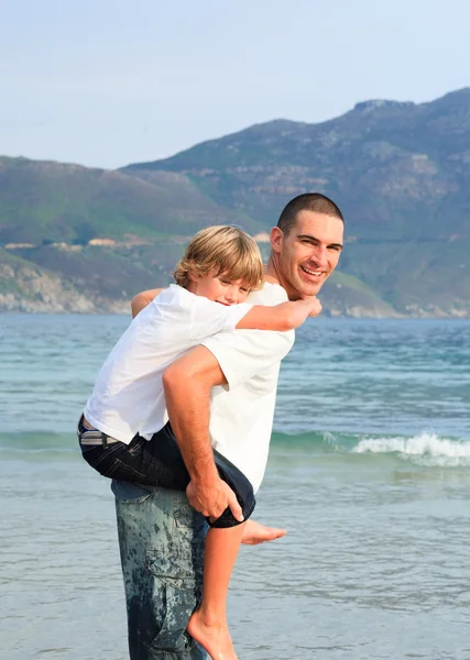 Father giving his son piggyback ride on the beach — Zdjęcie stockowe