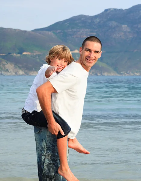 Vater gibt sohn huckepack fahrt auf die strand — Stockfoto