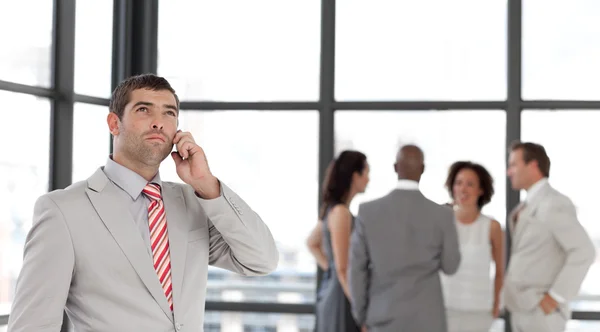 Hombre de negocios guapo en el teléfono en la oficina con su equipo — Foto de Stock