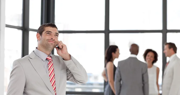 Knappe zakenman op telefoon op kantoor met zijn team — Stockfoto