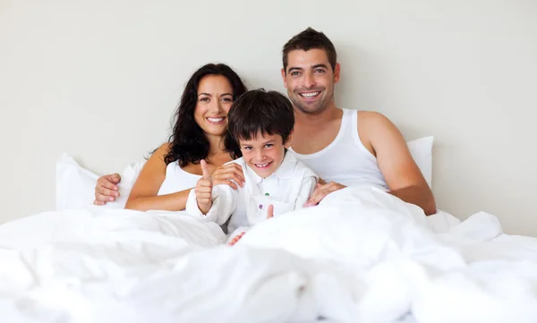 Criança com polegares para cima e seus pais na cama — Fotografia de Stock