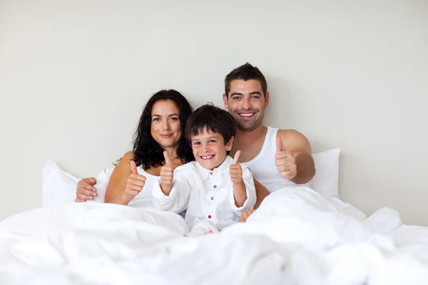 Başparmak yukarıya ve ailesi yatakta küçük çocuk — Stok fotoğraf