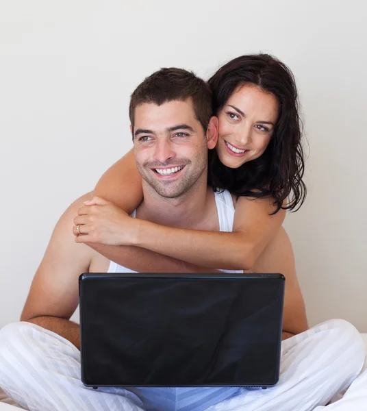 Casal encantador usando um laptop em uma cama — Fotografia de Stock