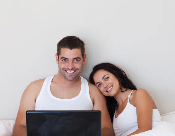 Ljusa par med en laptop på en säng — Stockfoto